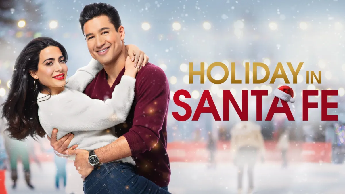 Official promotional title graphic for Holiday in Santa Fe featuring Mario Lopez holding Emeraude Toubia in a snowy ice-rink scene.