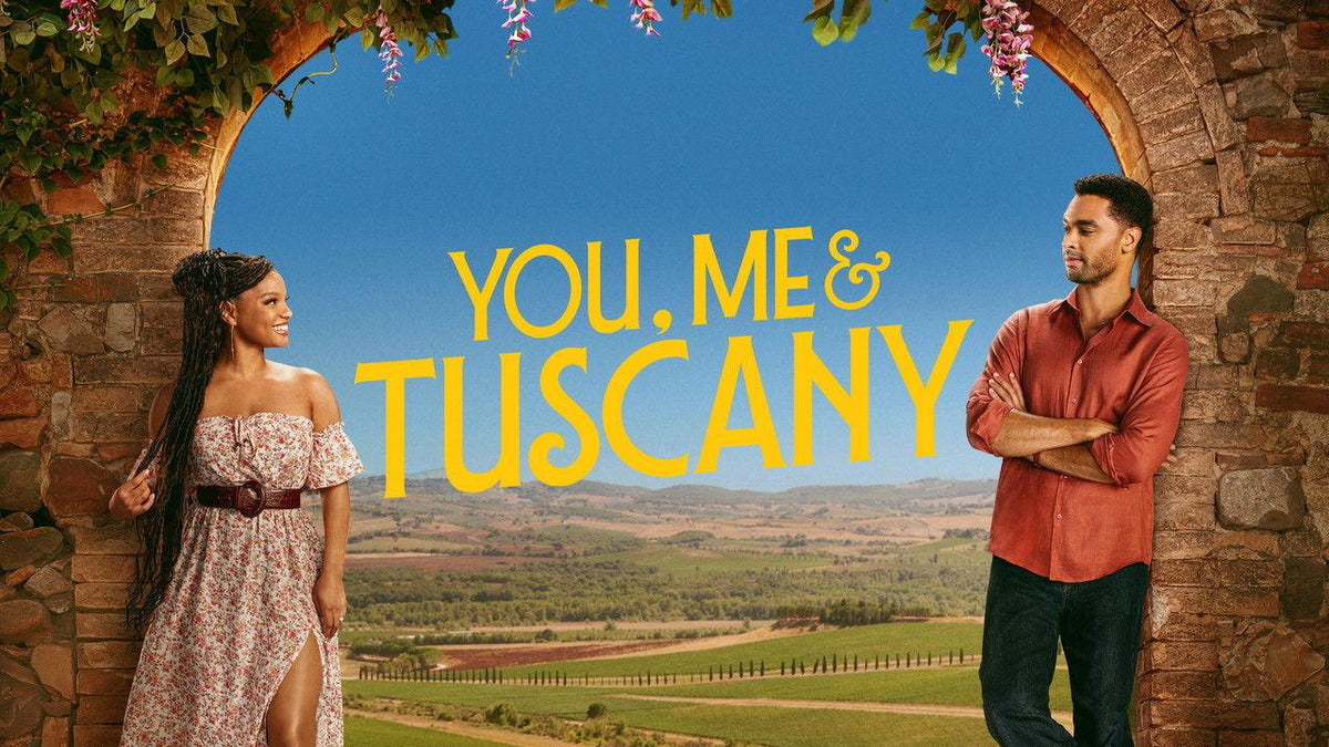 Official poster for You, Me & Tuscany featuring Halle Bailey and Regé-Jean Page leaning against a stone archway overlooking Tuscan hills.